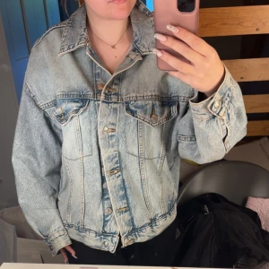 Oversized ljusblå jeansjacka - Säljer en oversized ljusblå jeansjacka med klassisk krage, bröstfickor med knappar och markerade sömmar. Jackan har långa ärmar och knäppning framtill. Perfekt för dig som gillar en avslappnad och trendig look.