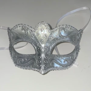 Silverfärgad maskeradmask med glitter - Snygg maskeradmask i silver med glittriga detaljer och vackra mönster. Masken har band att knyta bakom huvudet och passar perfekt till maskerad eller bal. Elegant design med swirl-mönster och metallic finish. Endast använd 1 gång så är i fint skick!! Hör av er vid frågor 💕💕