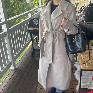 Beige kappa med bälte och krage - Lång beige kappa med bred krage och knytskärp i midjan. Klassisk och stilren modell med knappar framtill och långa ärmar. Perfekt för dig som vill ha en snygg och tidlös look under höst och vinter. Materialet känns mjukt och har en ullig känsla. strl xs me  passar även s. Kan va lite nopprig men inget störande alls💕