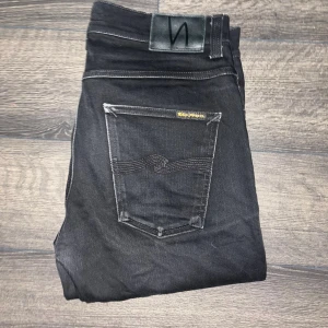 Nudie Jeans - Svarta jeans från Nudie Jeans, modell Lean Dean. Slimmad passform med raka ben och klassiska femficksdetaljer. Snygga kontrastsömmar och diskret logga på bakfickan. Midja 41cm, längd 108cm. JAG SKICKAR INGA FLER BILDER PÅ NÄR JAG BÄR PLAGGET:) s2