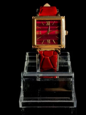 Velour Rouge - Velour Rouge är en elegant och stilfull armbandsklocka med en klassisk fyrkantig boett i guldfinish och en djup röd urtavla som ger ett exklusivt och sofistikerat uttryck. Det röda armbandet i läderlook kompletterar designen perfekt och gör klockan till ett riktigt statement-accessoar. Passar lika bra till vardag som till fest och är ett utmärkt val för dig som vill addera färg och elegans till din stil. Helt ny och i mycket fint skick. 