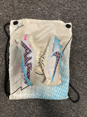 Nike Air Zoom Mercurial fotbollsskor - Säljer ett par Nike Air Zoom Mercurial fotbollsskor i vitt med blå och rosa detaljer. I storlek 38, endast använda en gång. 