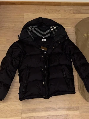 Burberry pufferjacket  - Säljer oanvänd burberry jacka med nytt skick. I storlek M, jackan kan bli till väst genom att dra av kedjorna vid armarna. Jackan kommer med dust bag, Pris kan diskuteras 