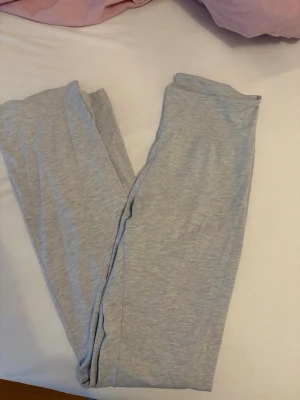 Ljusgrå yogapants - Säljer ett par ljusgrå yogapants med bred resår i midjan. Byxorna är tillverkade i mjukt bomullsmaterial och har en enkel, rak passform utan synliga detaljer eller mönster. Perfekta för chill eller träning hemma.