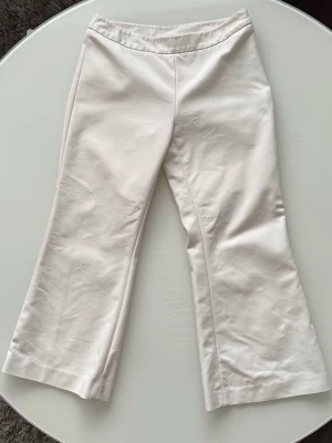 Vita bootcut byxor med dragkedja - Säljer ett par stilrena vita coulotte-byxor i bootcut-modell. Byxorna har en diskret dragkedja i sidan och är sydda i ett mjukt bomullsmaterial. Perfekta för dig som gillar minimalistisk och clean stil. Storlek S. 