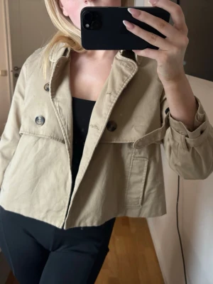 Beige trenchcoat med knappar - Intressekoll!!! Snygg trenchcoat i beige med dubbelknäppning. Perfekt för dig som vill ha en stilren och trendig jacka till vår eller höst.
