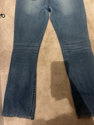Miss Me jeans bootcut ,midrise blå, storlek 33 1/2  - Säljer ett par blå jeans från Miss Me med bootcut passform. Jeansen har snygga broderade bakfickor med pärldetaljer och dekorativa nitar. Klassisk femficksmodell med slitningar och ljus tvätt. Dem är lite sönder vid bakfickorna som man kan se vid sista bilden. köpte för 1100 ,använt 1-3 gånger 