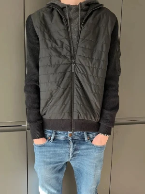 J Lindeberg Cardigan - Säljer en svart cardigan från J.Lindeberg med quiltad front och stickade ärmar. Den är i jättebra skick som ny, har inga hål eller ngt.  Perfekt nu inför våren. Nypriset på denna är runt 3k, mitt pris: 700