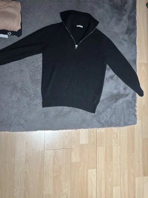 Svart ribbad stickad tröja Zara - Svart ribbad stickad tröja från Zara med hög krage och half zip-dragkedja. Långärmad modell i mjukt material som passar perfekt till kyligare dagar. Enkel och stilren design som är lätt att matcha. Hör av er vid minsta fundering!🙌