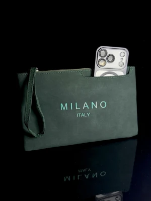 Milano Verde Pouch *Helt ny* - Elegant Milano pouch i stilren olivgrön nyans – helt ny och oanvänd. Perfekt både till vardag och resa. Smidig att använda som necessär eller som väska i väskan, lika praktisk för mindre utflykter som för större resor. Rymmer enkelt mobil, plånbok, pass, smink eller andra viktiga tillhörigheter. Tidlös och sofistikerad design som passar alla tillfällen. Unisex. I nyskick utan defekter.