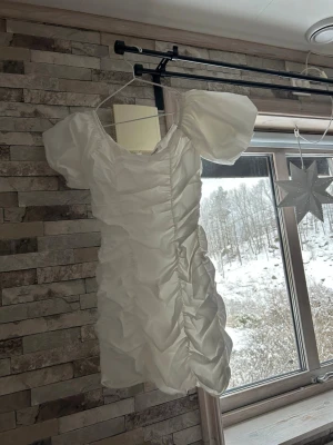 Vit kortklänning från Glamorous - Supersöt vit kortklänning från Glamorous med puffärmar och rynkade detaljer längs hela klänningen. Tillverkad i ett glansigt material som ger en lyxig känsla. Dragkedja i sidan för enkel påklädning. Perfekt för dig som vill sticka ut!