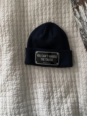 John hatter and co mössa - Säljer en marinblå mössa från John Hatter & Co med en stor metallbricka framtill där det står 'YOU CAN'T HANDLE THE TRUTH'. det är en fin mössa bra till vintern nu. Ny pris: 995kr mitt pris: 450kr