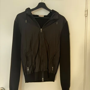 Svart Moncler hybridjacka med huva - Pris kan diskuteras! En svart moncler maglione tricot cardigan, som har stickade ärmar och rygg med en huva och framsida som är i ett mer vindjacks liknade material. Det är en äldre modell och säljer pågrund ut av att den inte kommer till användning så ofta och har mestadels hängt i min garderob i några år, har kommit till användning ca 8 gånger. 