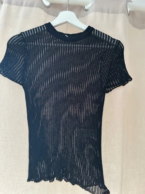 Svart transparent randig topp Zara - Säljer en svart transparent topp från Zara i storlek M. Toppen har korta ärmar, rund hals och ett vertikalt randigt mönster. Materialet är tunt och stretchigt, perfekt för att styla lager på lager. Snygg detalj med vågig kant nertill.