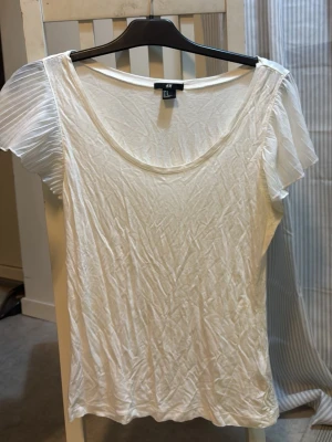 Vit blus med plisserade ärmar H&M - Säljer en vit blus från H&M i storlek M. Toppen har plisserade, korta ärmar i transparent material och en rund halsringning. Ärmarna ger en extra touch med sitt tunna, luftiga tyg.