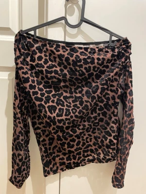 Leopardmönstrad offshoulder topp Gina Tricot - Säljer en snygg offshoulder topp från Gina Tricot i storlek S. Toppen har leopardmönster i svart och brun, är långärmad och gjord i ett tunt, stretchigt syntetmaterial. Perfekt för dig som vill sticka ut med en trendig look.