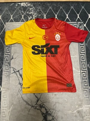 Galatasaray matchtröja Nike XS - Galatasaray matchtröja från Nike i storlek XS. Tröjan har klassisk halv gul och halv röd design med klubbmärke och fyra stjärnor på bröstet. Tillverkad i lätt polyester med Dri-FIT ADV-teknologi. Snygga tryck och detaljer, perfekt för fotbollsfans.
