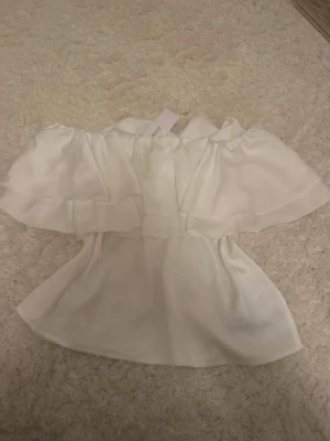 Vit offshoulder topp från Gina Tricot - Säljer en superfin vit offshoulder topp från Gina Tricot. Toppen har dubbla volanger över axlarna och är tillverkad i ett lätt, luftigt material som ger en romantisk vibe. Perfekt till sommarens alla tillfällen och enkel att styla med både jeans och kjol.