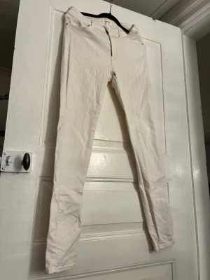 Vita skinny jeans från Mango - Säljer ett par vita skinny jeans från Mango med klassisk femficksdesign och bälteshällor. Byxorna har dragkedjegylf och knapp framtill. De är tillverkade i bomull med en smal passform som sitter tight längs benen. Perfekta att styla med sneakers eller boots. Skulle säga att de passar storlek S.