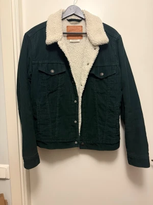 Mörkgrön Levi’s sherpajacka  - Säljer en mörkgrön klassisk fodrad Levi’s sherpajacka i manchester. Foder av polyester. Har mest hängt i garderoben de senaste åren och är i mycket gott skick! 