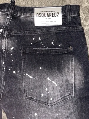 Svarta Dsquared2 jeans med färgstänk - Säljer ett par svarta jeans från Dsquared2 med coola vita färgstänk över hela byxorna. Jeansen har rak passform, klassisk femficksdesign och tydlig dragkedja framtill. Materialet är robust denim och de har en snygg tvättad look.