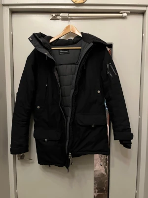 Svart parkas från Peak Performance dam (passar herr) M - Säljer en svart parkas från Peak Performance i dammodell men passar killar utmärkt, storlek M. Jackan har huva, flera praktiska fickor med både dragkedja och knappar samt mjukt foder. Perfekt för kalla dagar med sin långa passform och värmande material.