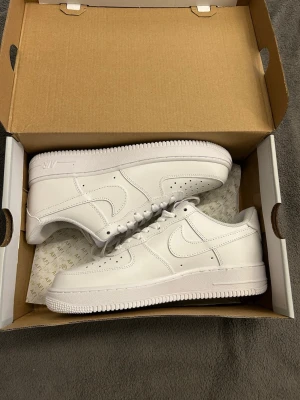 Nike Air Force 1 Low helvita sneakers - Nike Air Force 1 Low sneakers i helvit färg med klassisk siluett och rund tå. Skorna har snörning, perforerad tåbox och platt sula. Tillverkade i skinn med ikonisk swoosh på sidan. Perfekta för dig som gillar cleana och stilrena sneakers.