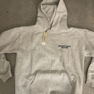 Essential Hoodie - Säljer en snygg och mycket populär Essentials (Fear of God) hoodie i en klassisk grå färg. Ett måste som passar perfekt till alla streetwear- eller vardagskläder. (Passar storlek M)  Mycket gott skick  Levereras med etikett och originalpåse  Hög kvalitet och superbekväm  Unisex passform  Snabb frakt tillgänglig - skickas snabbt efter köp  Först till kvarn!