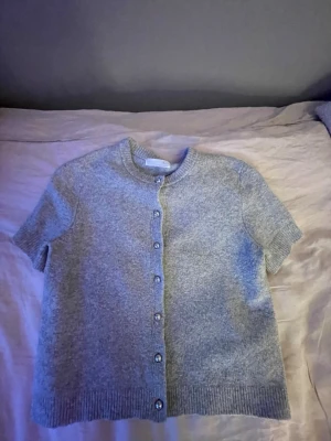 Grå kortärmad kofta från Primark - Kortärmad grå kofta från Primark. Koftan har knappar framtill och är gjord i mjukt stickat material. Perfekt att slänga över ett linne   💞 skriv för fler bilder eller hur den sitter på. Pris går att diskutera 🤍 använd ett fåtal gånger,säljer då den är lite liten för mig 💞