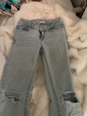 Ljusblå jeans med slitningar från Nelly - Ljusblå jeans från Nelly med bootcut och slitna hål vid knäna. Snygga detaljer med rosa sömmar och broderi på bakfickorna. 