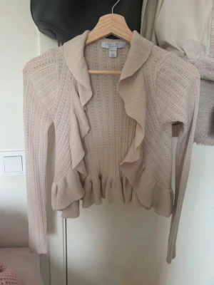 Beige volangkofta/bolero - Supersöt beige kofta från Amisu med volangdetaljer längs kanterna och nederdelen. Stickad i ett lätt material!