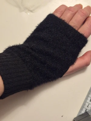  Helt nya Svart stickad handledsvärmare -  Helt nya Mysig svart handledsvärmare i fluffigt stickat material. Den har en enkel, clean look med ribbad mudd vid handleden och öppning för tummen. Perfekt för dig som vill hålla händerna varma men ändå ha fingrarna fria.