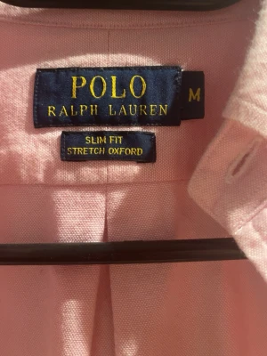 Rosa slim fit skjorta från Polo Ralph Lauren - Säljer en rosa stretch oxford-skjorta från Polo Ralph Lauren i slim fit. Skjortan har klassisk button-down krage, långa ärmar och knappar framtill. Ikoniska broderade loggan på bröstet. Perfekt för dig som gillar stilren och fräsch look. Använt 1 gång och 100% äkta 