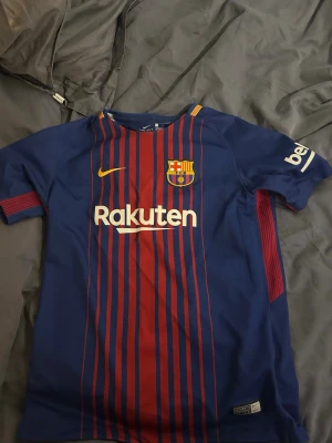 Barça Coutinho matchtröja Nike L - Säljer en FC Barcelona matchtröja från Nike med Coutinho och nummer 14 på ryggen. Tröjan är blå och vinröd med gula detaljer, tillverkad i Dri-FIT polyester. Klassiska ränder framtill, klubbmärke och sponsortryck. Perfekt för dig som älskar fotboll och Barça. Finns små defekter på magen som man knappt märker av 