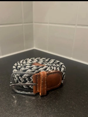 Flätat bälte  - Svart vitt grå flätat bälte  Töjbart och skönt  Storlek: 120cm töjbart  Bruna detaljer   MER MÄRKESKLÄDER I PROFILEN