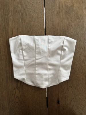 Vit korsettopp från Nelly - Snygg vit korsettopp från Nelly i satinliknande material och snörning i ryggen. Storlek S 