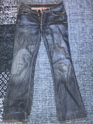 Bootcut jeans från H&M, blå 28/32 - Snygga blå bootcut jeans från H&M i 100% bomull. Klassisk femficksmodell med knäppning framtill och kontrastsömmar. Jeansen har en mörk tvätt och en avslappnad bootcut-passform som ger en retrovibe. Jeansen är pytte lite slitna där nere vid hällarna men inga hål !!!
