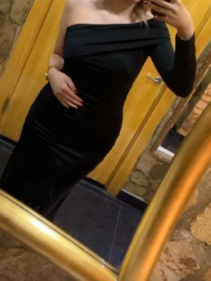 Svart oneshoulder långklänning - Säljer en elegant svart långklänning med oneshoulder-design och lång ärm på ena sidan. Klänningen har en figurnära passform och draperad detalj över bysten. Perfekt för dig som vill sticka ut med en stilren look. Använd en gång sitter tajt och formar kroppen fint.