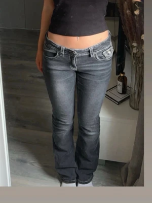 Svarta bootcut jeans  - Säljer ett par svarta jeans med bootcut passform och vita kontrastsömmar. Byxorna har låg midja, klassiska fem fickor och snygga detaljer på bakfickorna med lock och knapp. Perfekta för dig som gillar en retro vibe och vill ha något som sticker ut. Storlek 164 men passar även S