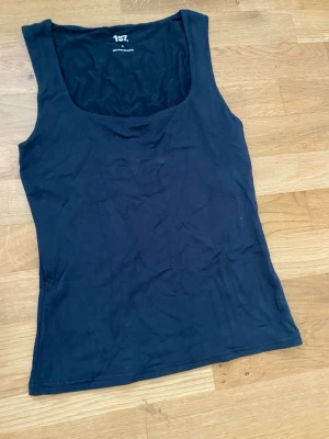 Svart linnetopp från 157, storlek S - En enkel och stilren svart linnetopp från 157 i storlek S. Toppen är ärmlös med breda axelband och rundad urringning. Tillverkad i mjuk och stretchig viskosblandning för skön passform. Perfekt att matcha med jeans eller kjol.