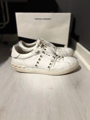 Valentino open  - Säljer ett par vita Valentino open Rockstud sneakers i skinn med ikoniska nitar längs sidorna och runt hälen. Skorna har snörning, platt sula och en clean, stilren look med edgy detaljer. Perfekta för dig som vill ha något lyxigt och unikt i garderoben.