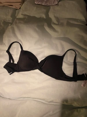 Svart push up bikiniöverdel 34 - Säljer en svart push up bikiniöverdel i storlek 34. Enkel och stilren design med justerbara axelband och smidig knäppning bak. Materialet är mjukt och följsamt, perfekt för strand eller poolhäng.