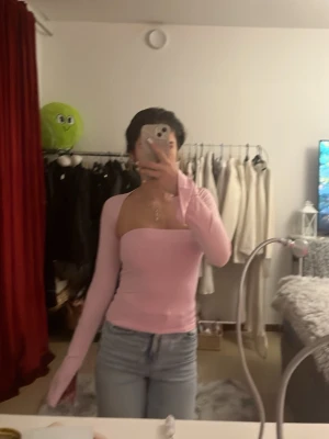 Ljusrosa långärmad topp - Säljer en ljusrosa långärmad topp med axelbandslös design och tight passform. Toppen har raka linjer över bysten och är tillverkad i ett mjukt, stretchigt material som sitter snyggt på kroppen. Perfekt att styla med jeans eller kjol.