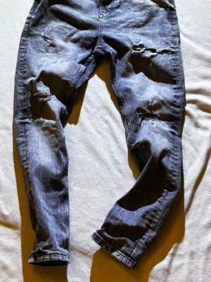 Grå slitna jeans från FSBN - Säljer ett par grå jeans från FSBN med slitningar och hål på båda benen för en riktigt edgy look. Jeansen har normal passform, klassisk femficksdesign och är tillverkade i mjukt bomullsmaterial. Perfekta för dig som gillar streetstyle och vill sticka ut.