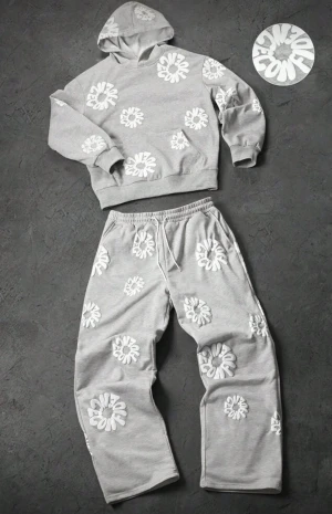 Grå mjukisbyxor och hoddie - Säljer ett par grå mjukisbyxor med elastisk midja och snörning. Byxorna har vita, broderade textmönster över hela plagget som ger en cool och unik look. Perfekta för chill dagar eller när du vill ha något bekvämt men ändå snyggt.