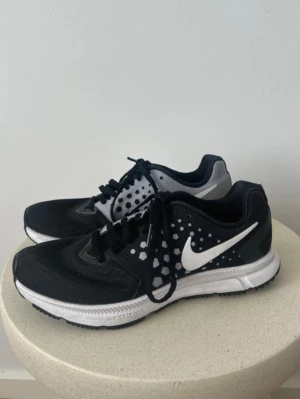 Nike Zoom löparskor svart/vit - Nike Zoom löparskor i svart och vitt med hexagonmönster på sidorna och stor vit Swoosh. Mellansulan är vit med texten 'Nike Zoom' och yttersulan är svart. Perfekta för löpning eller träning. Storlek 36.5. Fint skick 🖤