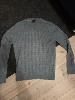 Grå stickad tröja Massimo Dutti - Säljer en grå stickad tröja från Massimo Dutti i klassisk modell. Tröjan har ett ribbat mönster, rund halsringning och långa ärmar. Perfekt till höst och vinter när du vill vara både stilren och bekväm.