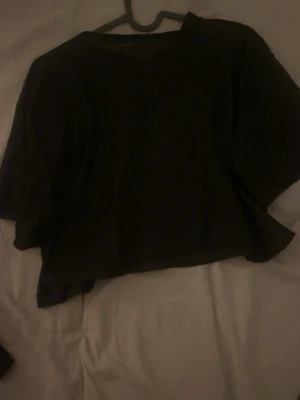 Svart mesh croppad topp - Säljer en svart mesh topp med croppad passform. Toppen är genomskinlig och har vida, korta ärmar. Perfekt att styla över ett linne eller bralette för en cool och edgy look. Materialet är lätt och luftigt syntet.