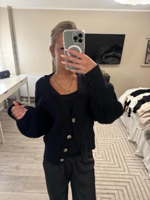 Svart stickad kofta med knappar - Säljer en svart stickad kofta med stora, snygga knappar framtill. Koftan har v-ringning och långa, lite puffiga ärmar. Perfekt att slänga på sig över ett linne eller t-shirt för en chill look.