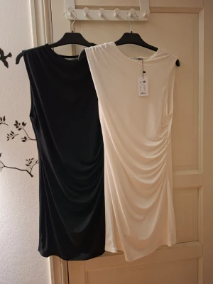 Svart och vit kortklänning med drapering - Två stilrena kortklänningar , en i svart och en i vit. Båda är ärmlösa med rund halsringning och har snygg drapering på ena sidan som ger en cool och modern look. Materialet känns mjukt och stretchigt, perfekt för dig som gillar minimalistisk stil. 100kr st 